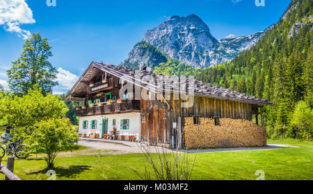 Panoramic view of idyllic mountain scenery in the Alps with traditional farmhouse and fresh green mountain pastures in summer Stock Photo