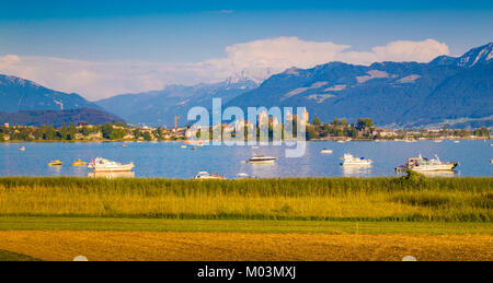 Beautiful view of boats lying in Lake Zurich with the historic town of Rapperswil in the background in golden evening light at sunset, Rapperswil-Jona Stock Photo