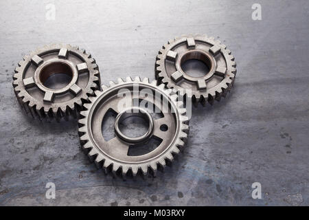 A group of solid metal gears are linked together on a grungy steel background. This set of industrial cog wheels can be used to represent the concept  Stock Photo