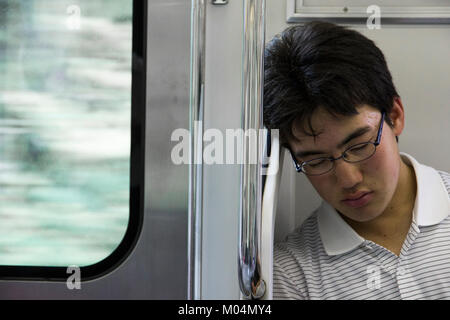Young Japanese male student sleeping inside a train in Tokyo, Japan, close to a window Stock Photo