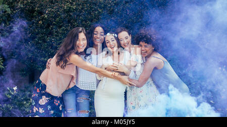 Group of happy female friends hugging pregnant woman outdoors. Expecting mother and her friends with smoke grenade at baby shower. Stock Photo