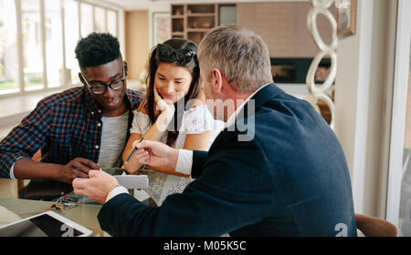 Real estate agent showing detail of  lease agreement to interracial couple. Estate broker explaining lease agreement or purchase contract to couple in Stock Photo