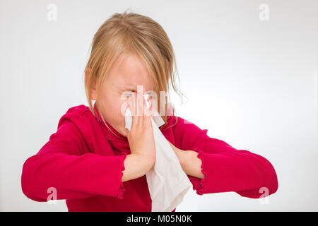A girl is biting into a white handkerchief. She is 7 years old and wears a red pullover Stock Photo