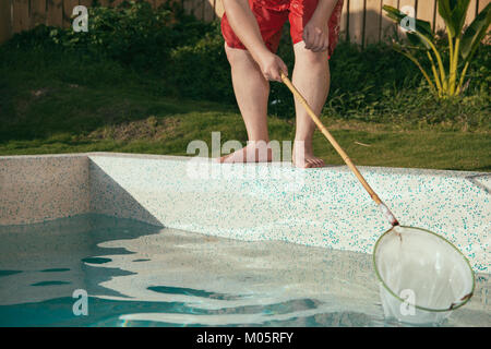 man using net tool scoop up leaf or dirty thing and cleaning swimming tool to maintain clean. Stock Photo