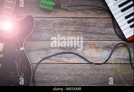 Black electric guitar, effect pedal and keyboard on a rustic wooden background, light glow Stock Photo