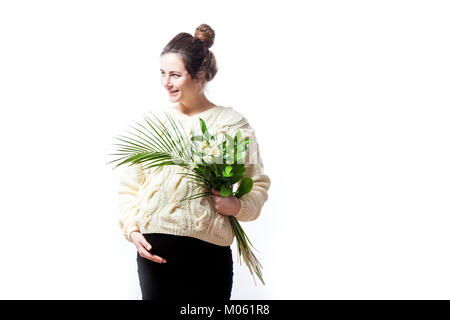 A young beautiful woman in a knitted sweater and a black dress on her last pregnancy holds a bouquet of flowers of irises in her hands and smiles on a Stock Photo