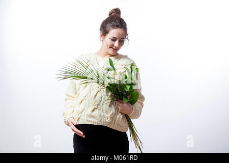 Young cheerful dark-haired woman in a knitted sweater and a black dress on her last pregnancy holds a bouquet of flowers of irises in her hands, posin Stock Photo