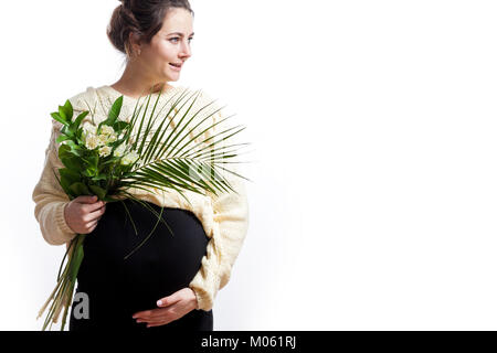 Young cheerful dark-haired woman in knitted sweater and black dress on late pregnancy holds a bouquet of flowers and smiling on white isolated backgro Stock Photo