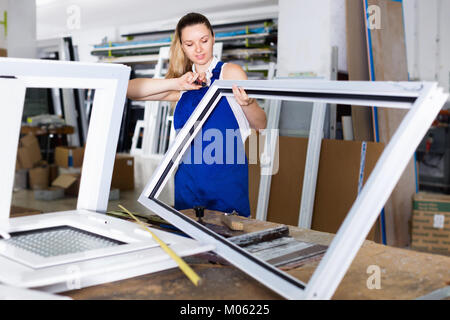 Diligent efficient positive  workwoman assembling PVC window in workshop with manual tools Stock Photo