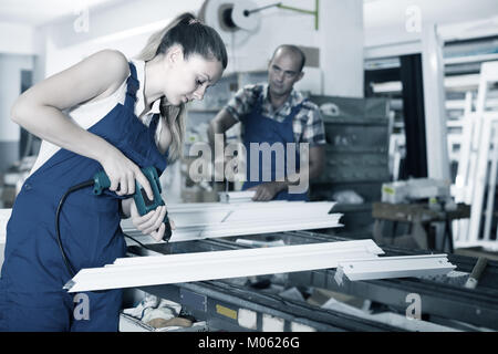 Craftswoman is assembling metal-plastic window in workshop, using electric drill. Stock Photo