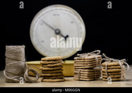 Samoyed cakes tied in bundles and kitchen scale. Cookies on a wooden kitchen table. Black background. Stock Photo