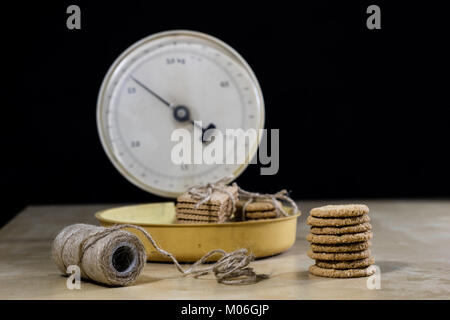 Samoyed cakes tied in bundles and kitchen scale. Cookies on a wooden kitchen table. Black background. Stock Photo