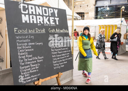 Stall owner walking in front of a billboard promoting the Canopy Market, King's Cross, London. Canopy market is a pop-up market near Granary Square wh Stock Photo