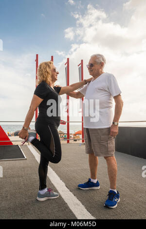Model Released - Mature heterosexual couple exercising together. Man supporting woman while she stretches her quadriceps Stock Photo