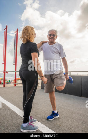 Model Released - Mature heterosexual couple exercising together. Woman supporting man while stretching his quadriceps Stock Photo