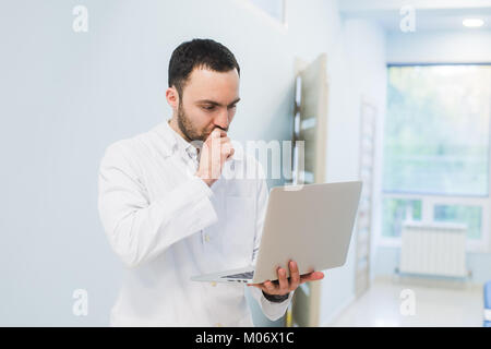 Portrait of cheerful doctor sitting at the desk working on laptop Stock Photo