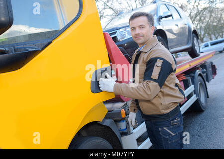 portrait of a tow truck woker with a towed car Stock Photo