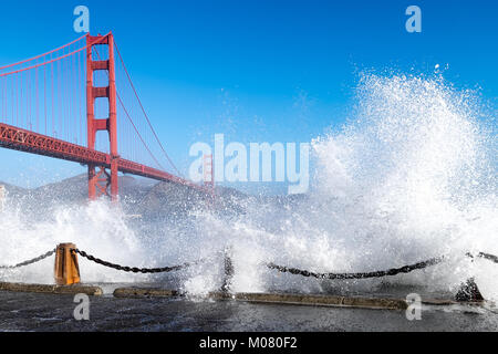 Golden Gate Bridge view framed by huge waves crashing over a sea wall below the bridge. Stock Photo