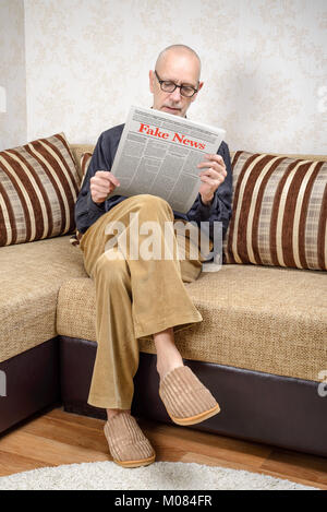 A man wearing glasses is sitting on a couch at home, reading a newspaper reporting fake news. Fake Lorem ipsum text. Stock Photo