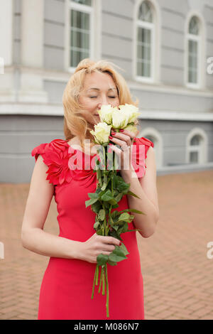 Woman in red dress sniffs white roses Stock Photo