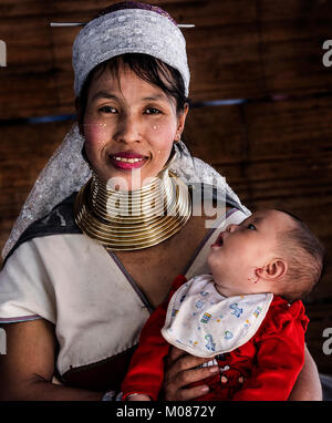 Portrait of long neck tribal mother and her baby sitting outside house, Thailand Stock Photo