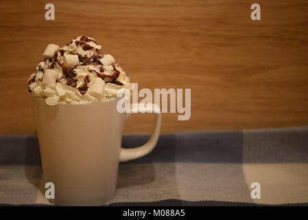 food and drink photography image of a fresh hot chocolate drink in a white mug or cup topped with whipped cream mini marshmallows and chocolate Stock Photo