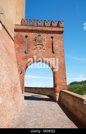 Barolo medieval castle entrance arch in red bricks and emblem with empty street and green vineyards in a sunny summer day Stock Photo