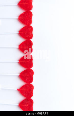 Heart shaped red valentine lollipops in row along left side with white background Stock Photo