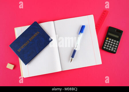 A blue book with an inscription in Russian - a student's record book. Pen, calculator and blank notebooks on a pink background. Students' Day Stock Photo