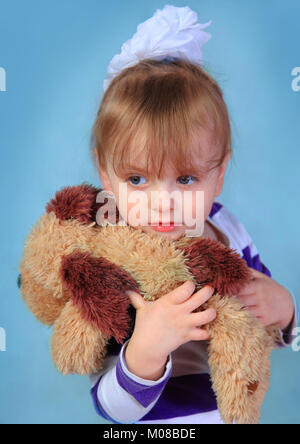 Portrait of a beautiful little girl on a blue background with a soft toy dog in hand, she hugs her, gaze directed towards Stock Photo