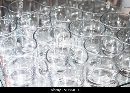 Array of shot glasses on white table - metallic colors. Glasses side by side and reflecting into each other. Stock Photo