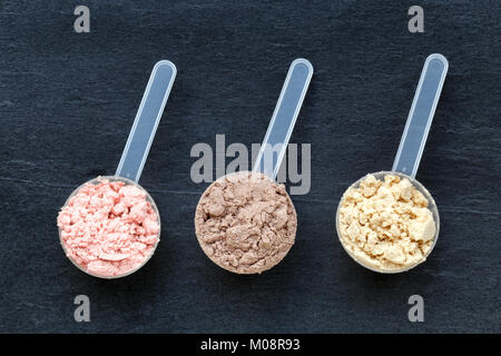 Plastic measuring spoons filled with whey protein powder against dark background Stock Photo