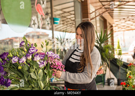 Small business concept. Smilng female florist picking flowers in a flower shop. Horizontal composition Stock Photo