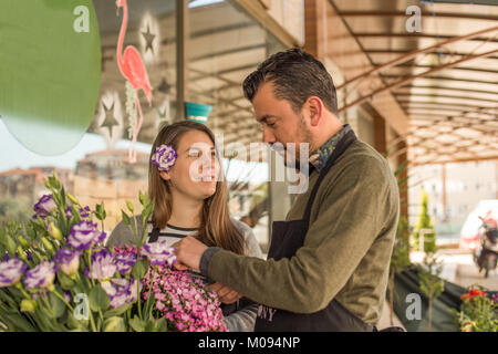 Small business concept. Male florist picking flowers and female florist with lisianthus in her hair looking at him with smile. Stock Photo