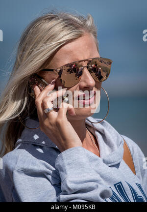 Blonde Highlighted Girl wearing shades, talking whilst on her mobile. Stock Photo