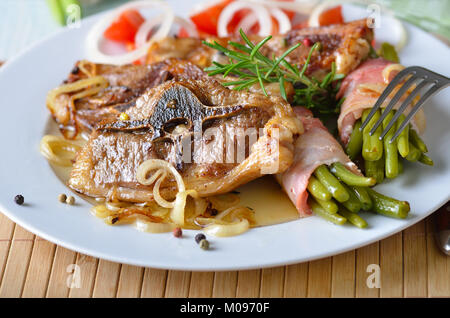 Fried lamb chops with onions and bacon-wrapped green beans Stock Photo