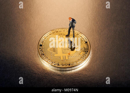 Businessman miniature figure standing on a gold Bitcoin looking down thinking about the risks and returns of investing in the cryptocurrency Stock Photo