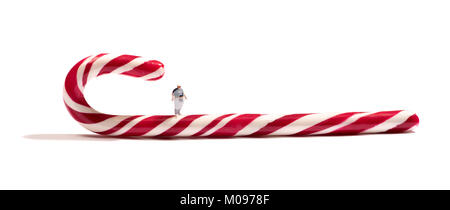 Miniature fat boy figure standing on a striped candy cane in a concept of an unhealthy diet and obesity with copy space on white Stock Photo