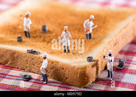 Group of miniature cooks or chefs on a slice of white toast in a concept of teamwork in preparing food and catering Stock Photo