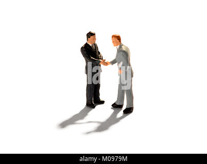 Two miniature figures of businessmen shaking hands as they clinch a deal or reach an agreement over a white background with shadows Stock Photo