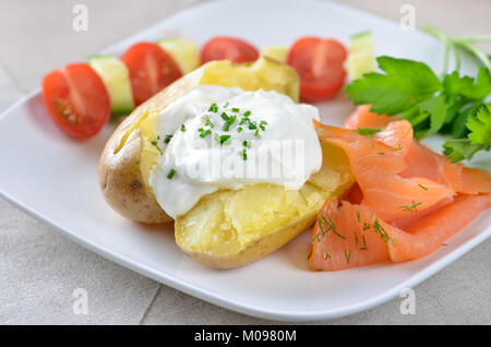 Jacket potato with sour cream, herbs  and smoked salmon, tomatoes and cucumber Stock Photo