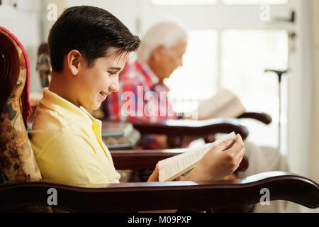 Grandson And Grandpa Reading Book And Relaxing At Home Stock Photo