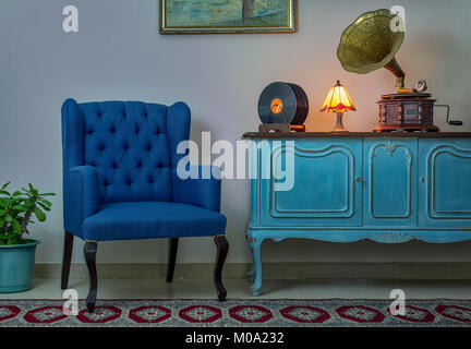 Interior shot of blue armchair, vintage wooden light blue sideboard, lighted antique table lamp, old phonograph (gramophone), vinyl records Stock Photo