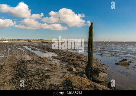 A wooden post with some clouds, seen at the Oare Marshes near Faversham, Kent, England, UK - with some boats and the Isle of Sheppey in the background Stock Photo