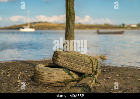 Old tyres and a wooden post in the Oare Marshes near Faversham, Kent, England, UK - with boats and the Isle of Sheppey in the background Stock Photo