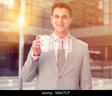 Portrait of young successful businessman drinking coffee near large factory Stock Photo