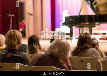 audience listening as Little girl is playing on a big black piano. selective focus Stock Photo
