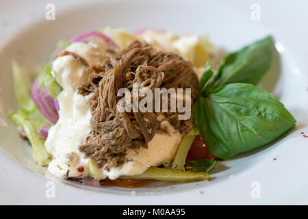 Warm salad with beef, tomato and lettuce leaves on white plate Stock Photo