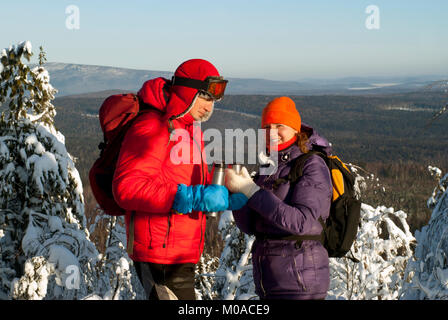 two hikers stand on top of the mountain in winter and drink hot tea from a thermos Stock Photo