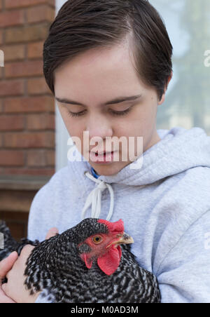 Attractive teenage boy with Autism and Down's Syndrome holding a barred rock hen outside Stock Photo